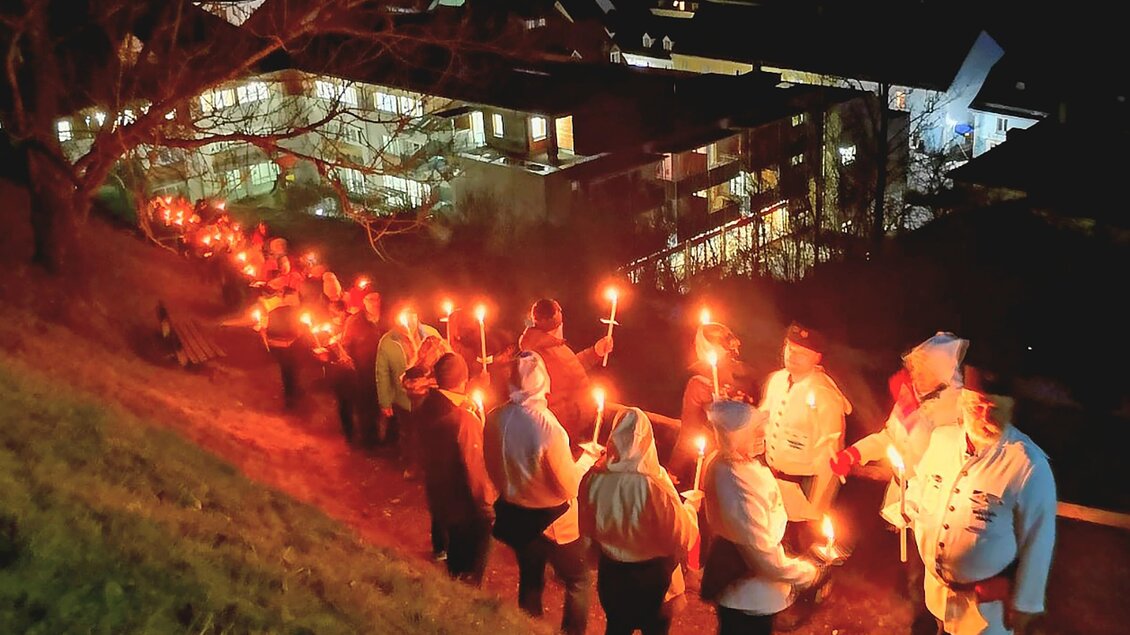 Eine Gruppe von Menschen steht in einer Reihe und hält Fackeln in der Nacht. Im Hintergrund sind beleuchtete Gebäude sichtbar. | © Schaubergwerk Oberzeiring