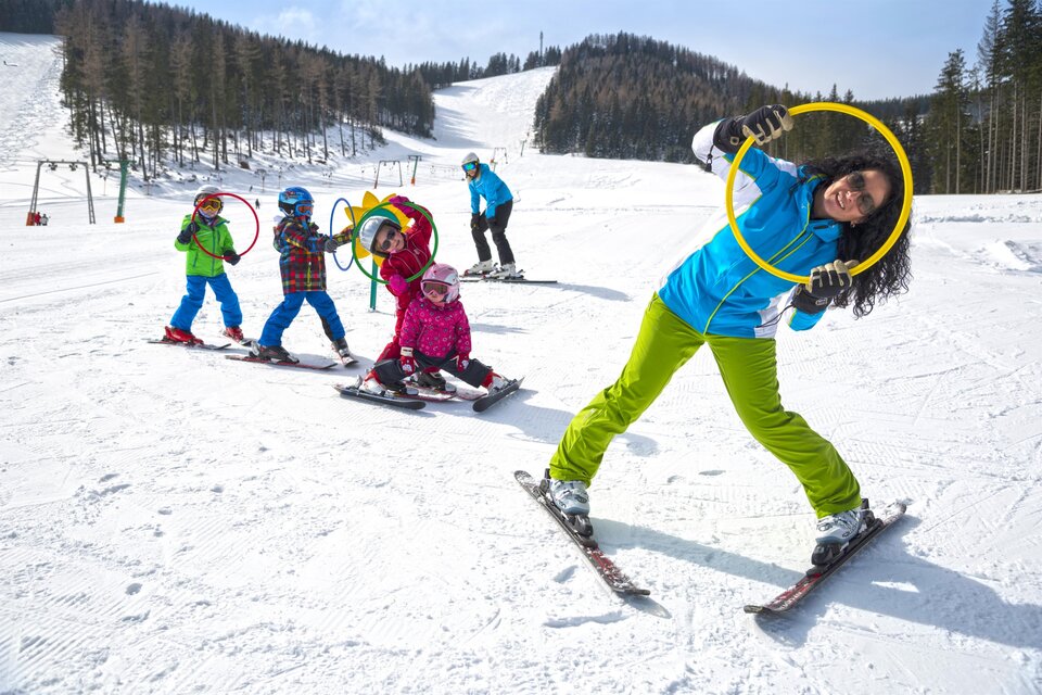 Eine Gruppe von Kindern und einem Erwachsenen fährt Ski im Schnee. Die Kinder haben Spaß mit Reifen auf der Piste. | © Tourismusverband Oststeiermark