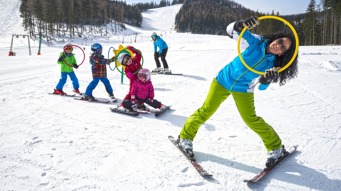 Eine Gruppe von Kindern und einem Erwachsenen fährt Ski im Schnee. Die Kinder haben Spaß mit Reifen auf der Piste. | © Tourismusverband Oststeiermark