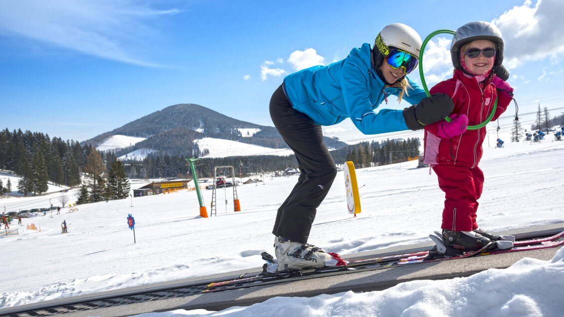 Ein Kind und ein Erwachsener stehen auf Skiern in einem Winterlandschaft. Im Hintergrund sind schneebedeckte Berge und ein klarer Himmel zu sehen. | © Tourismusverband Oststeiermark