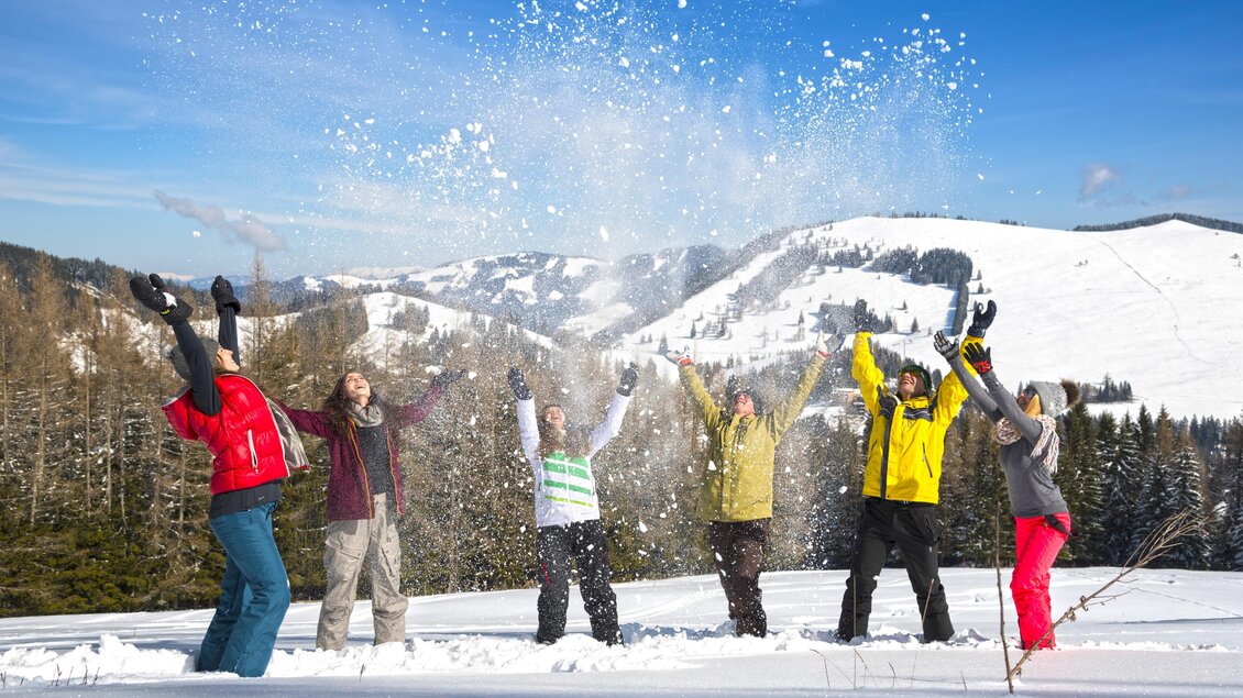 Eine Gruppe von Menschen steht im Schnee und hat Spaß. Sie werfen Schnee in die Luft und genießen den Wintertag. | © Tourismusverband Oststeiermark