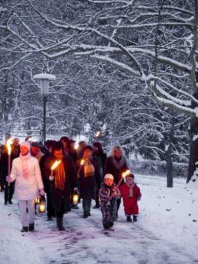 Eine Gruppe von Menschen geht im Schnee spazieren und trägt Laternen. Die Bäume sind mit Schnee bedeckt und die Atmosphäre ist festlich. | © TVB Thermen- & Vulkanland