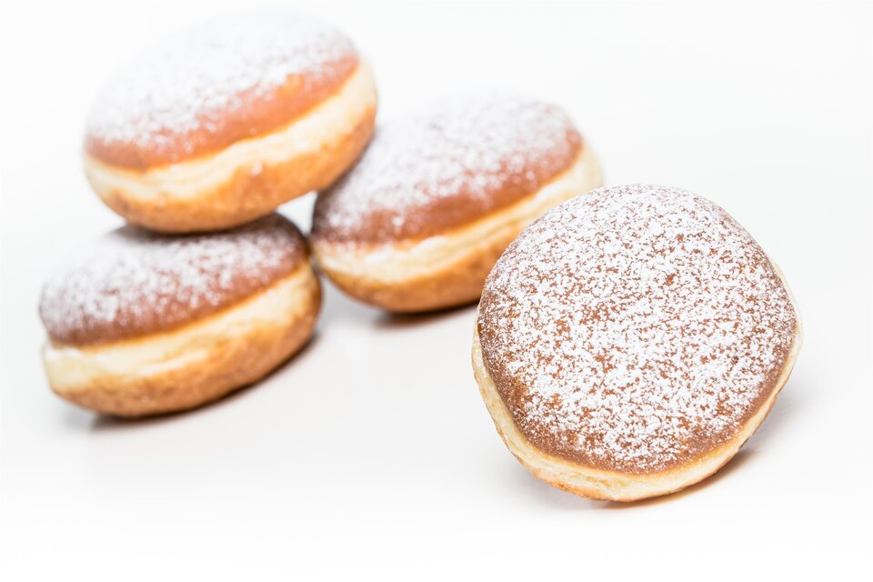 Eine Gruppe von leckeren, mit Puderzucker bestäubten Krapfen. Die Krapfen sind goldbraun und auf einem weißen Hintergrund angeordnet. | © Bäckerei Felber