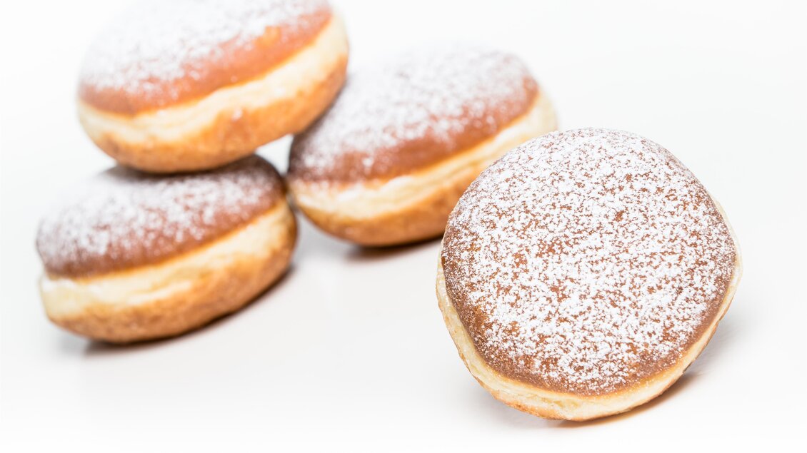 Eine Gruppe von leckeren, mit Puderzucker bestäubten Krapfen. Die Krapfen sind goldbraun und auf einem weißen Hintergrund angeordnet. | © Bäckerei Felber