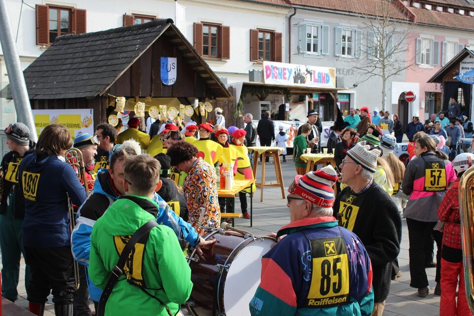 Eine bunte Menschenmenge versammelt sich auf einer Straße, während sie sich auf ein Fest vorbereitet. Lebhafte Kostüme und musikalische Elemente schaffen eine fröhliche Atmosphäre. | © Stadtgemeinde Fehring