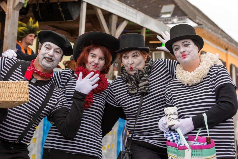 Eine Gruppe von vier Menschen in gestreiften T-Shirts und Zylindern posiert fröhlich. Sie sind als Pantomimen geschminkt und halten verschiedene Requisiten in den Händen.