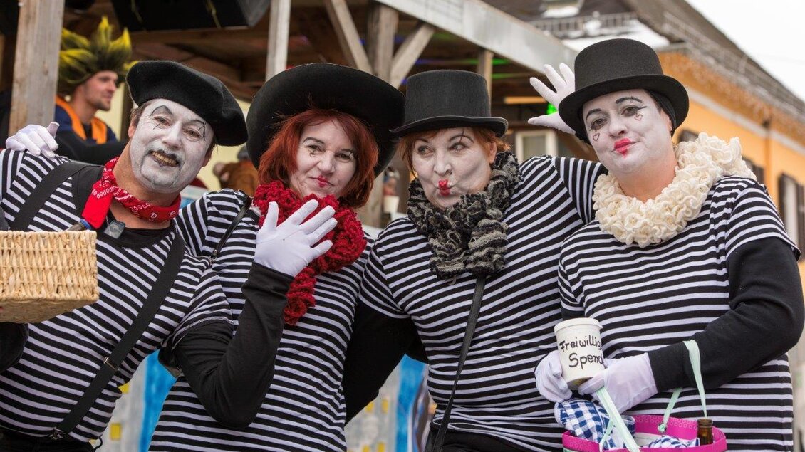 Eine Gruppe von vier Menschen in gestreiften T-Shirts und Zylindern posiert fröhlich. Sie sind als Pantomimen geschminkt und halten verschiedene Requisiten in den Händen.