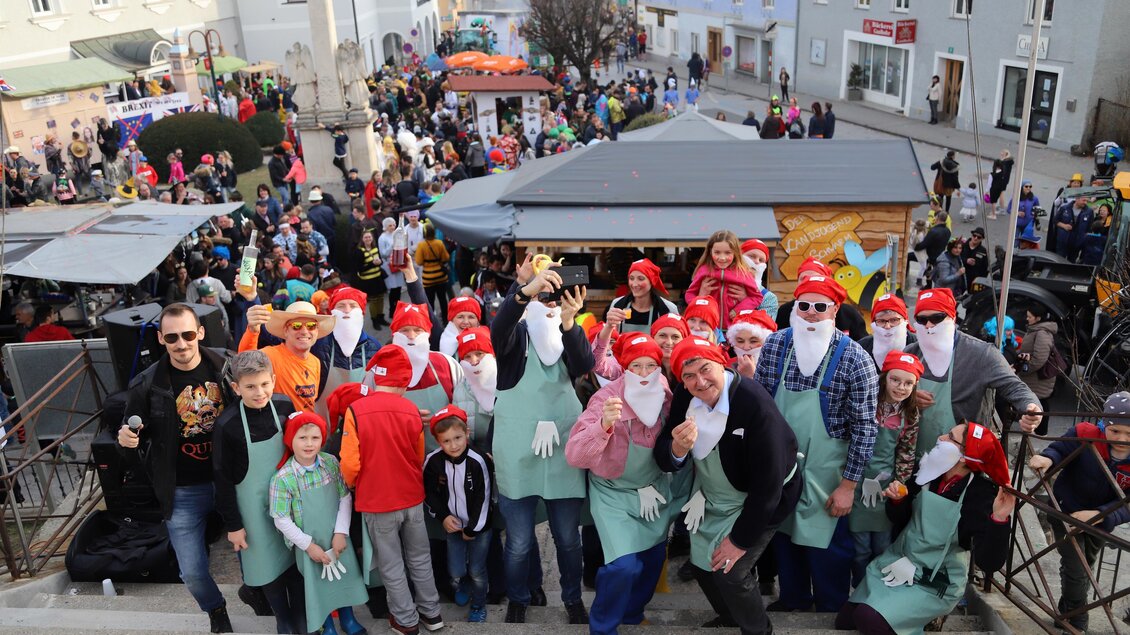 Eine fröhliche Gruppe von Menschen in Weihnachtsmannkostümen versammelt sich auf einer Treppe. Im Hintergrund sind zahlreiche Feiernde und festlich geschmückte Stände zu sehen. | © Oststeiermark Tourismus