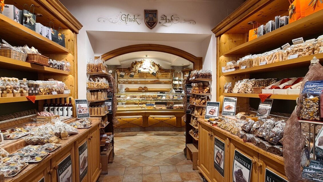 Ein einladendes Geschäft mit Holzregalen voller süßer Leckereien und Snacks. Im Hintergrund sind weitere Köstlichkeiten in der Verkaufstheke sichtbar. | © Stephanie Bor