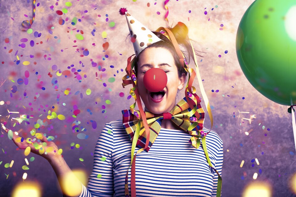 Eine fröhliche Person mit einer Clownsnase und einem Partyhut steht inmitten von Konfetti. Sie lächelt und hat bunte Luftballons um sich herum. | © TV Südsteiermark - Drubig-Photo