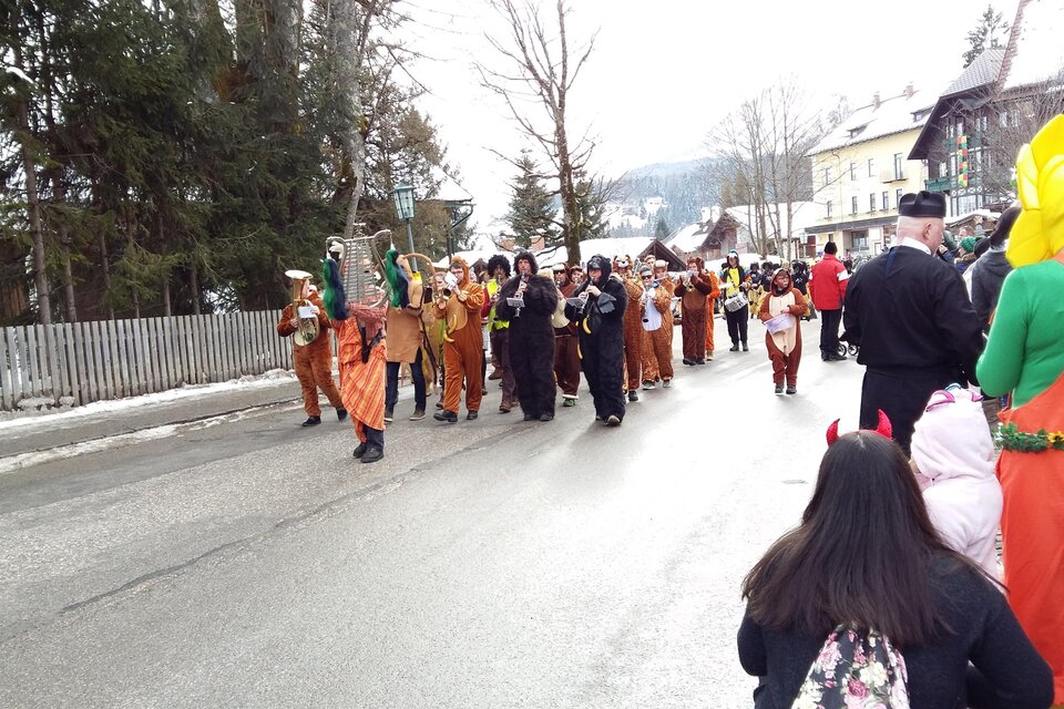 Eine bunte Gruppe von Menschen in Kostümen marchiert auf einer Straße. Im Hintergrund sind verschneite Bäume und Häuser zu sehen. | © Kirchschlager Petra