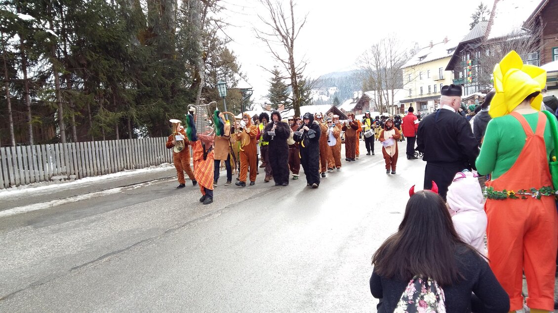 Eine bunte Gruppe von Menschen in Kostümen marchiert auf einer Straße. Im Hintergrund sind verschneite Bäume und Häuser zu sehen. | © Kirchschlager Petra