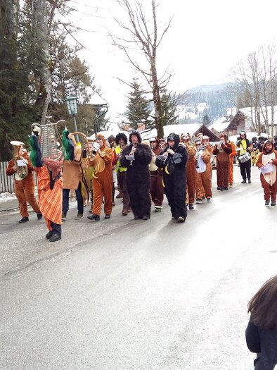 Eine bunte Gruppe von Menschen in Kostümen marchiert auf einer Straße. Im Hintergrund sind verschneite Bäume und Häuser zu sehen. | © Kirchschlager Petra