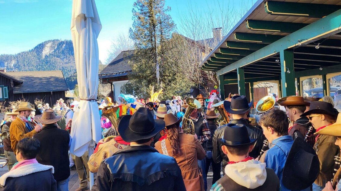 Eine bunte Versammlung von Menschen in Hüten und Kostümen feiert im Freien. Im Hintergrund sind Berge und ein klarer Himmel zu sehen. | © Petra Kirchschlager