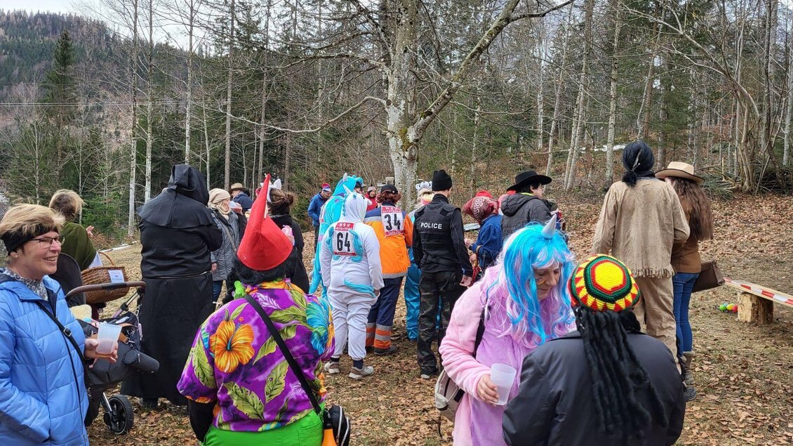 Eine Gruppe von Menschen feiert im Freien, viele tragen bunte Kostüme. Im Hintergrund sind Bäume und eine natürliche Landschaft zu sehen. | © Petra Kirchschlager