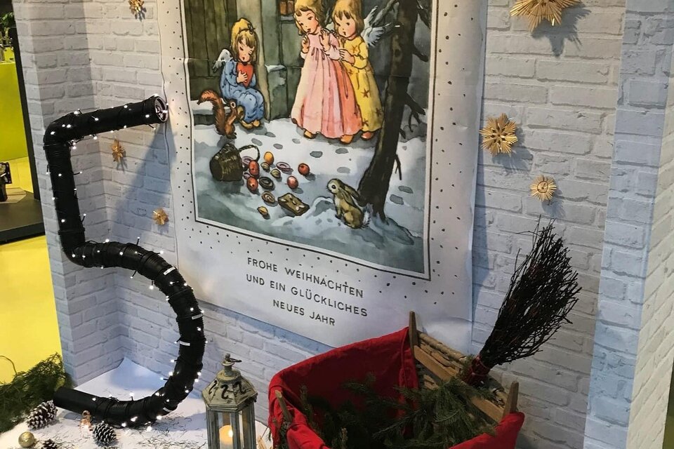 Ein weihnachtlich dekorierter Raum mit einer großen Wandmalerei von zwei Mädchen im Schnee. Im Vordergrund steht ein roter Korb, umgeben von Tannenzweigen und einer großen Zahl fünf. | © Stadtgemeinde Fehring
