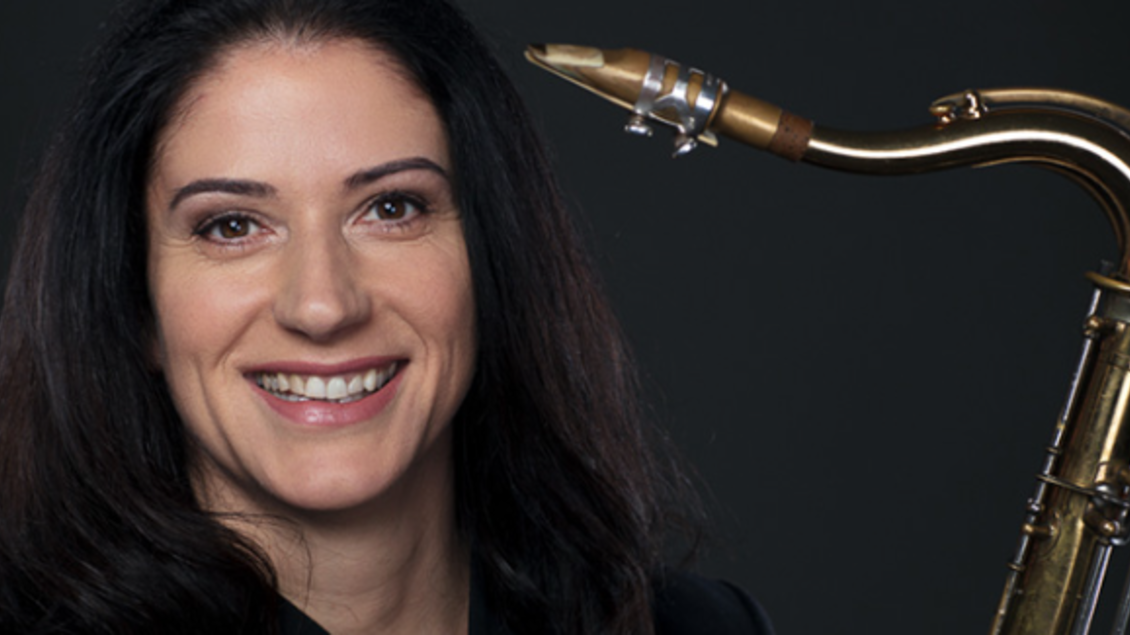 Eine Frau lächelt und hält ein Saxophon in der Hand. Der Hintergrund ist dunkel und hebt die Instrumenten hervor. | © ©Maria Frodl