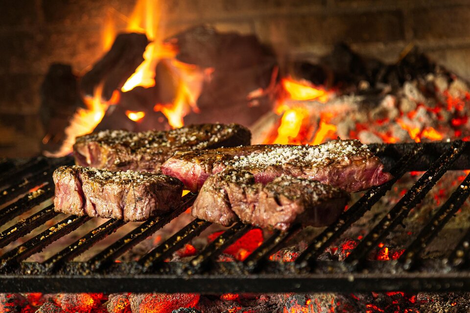 Saftige Steaks, die über offenem Feuer grillen. Im Hintergrund lodern die Flammen und glühen die Kohlen. | © Naturwelten Steiermark
