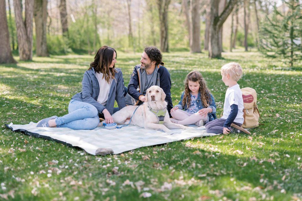 Eine Familie sitzt auf einer Decke im Park und genießt die Zeit miteinander. Neben ihnen liegt ein Hund auf dem Gras. | © Tourismusverband Oststeiermark