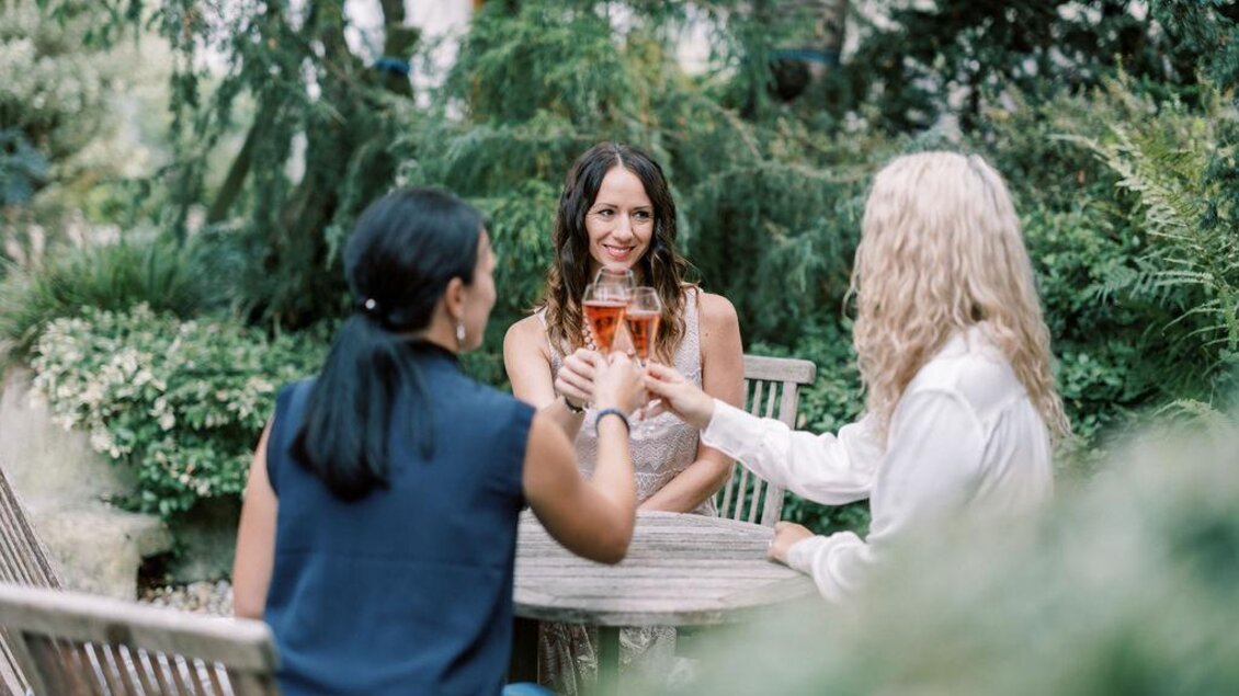 Drei Frauen stoßen an einem Tisch im Garten an. Sie lächeln, während sie Gläser mit Getränken halten. | © Tourismusverband Oststeiermark