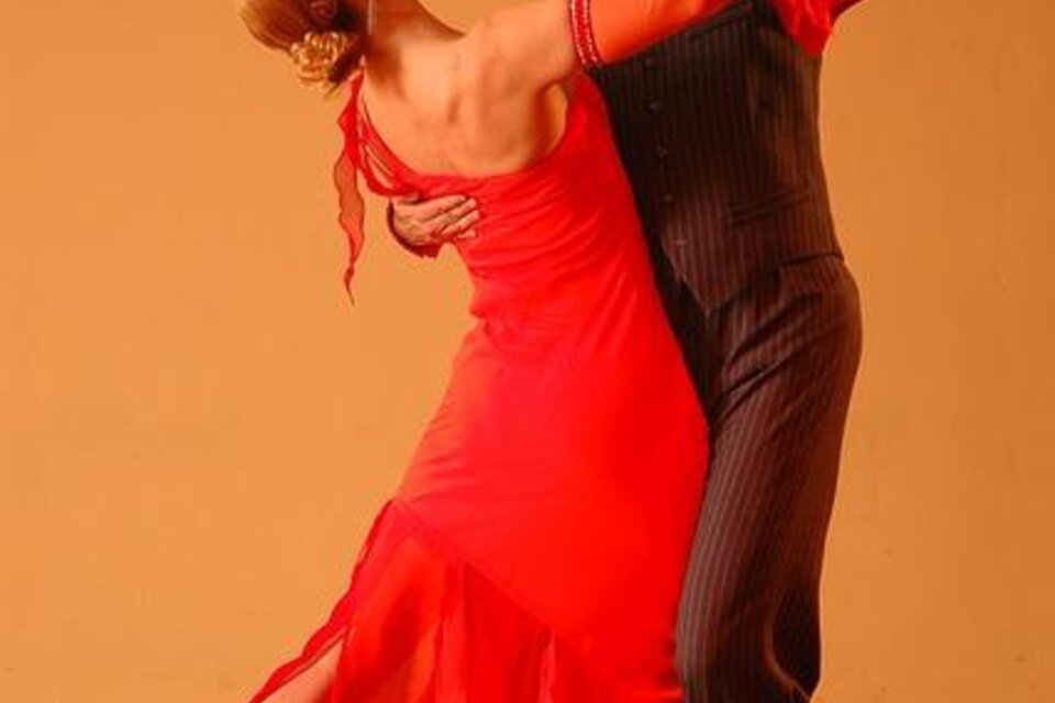 Ein Paar tanzt leidenschaftlich Tango. Die Frau trägt ein rotes Kleid und der Mann ist elegant gekleidet.