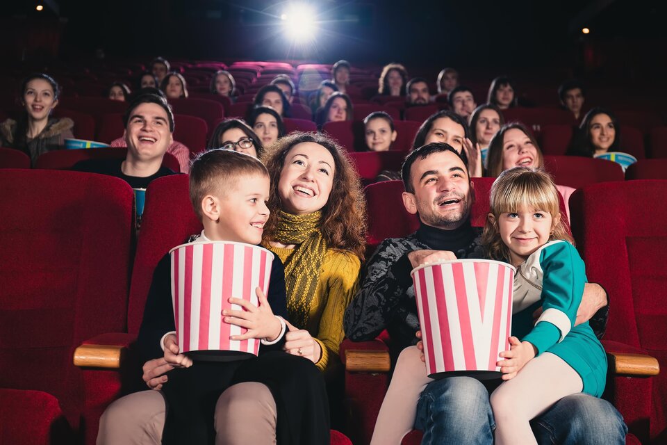 Eine fröhliche Familie sitzt im Kino und schaut einen Film. Alle halten Popcorn in den Händen und genießen den Abend. | © AdobeStock_162889360