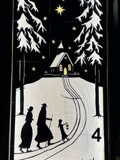 A wintry scene with two people and a child walking on a snow-covered path to a small church. Surrounded by fir trees and a clear night sky with twinkling stars. | © Elisabeth Winter