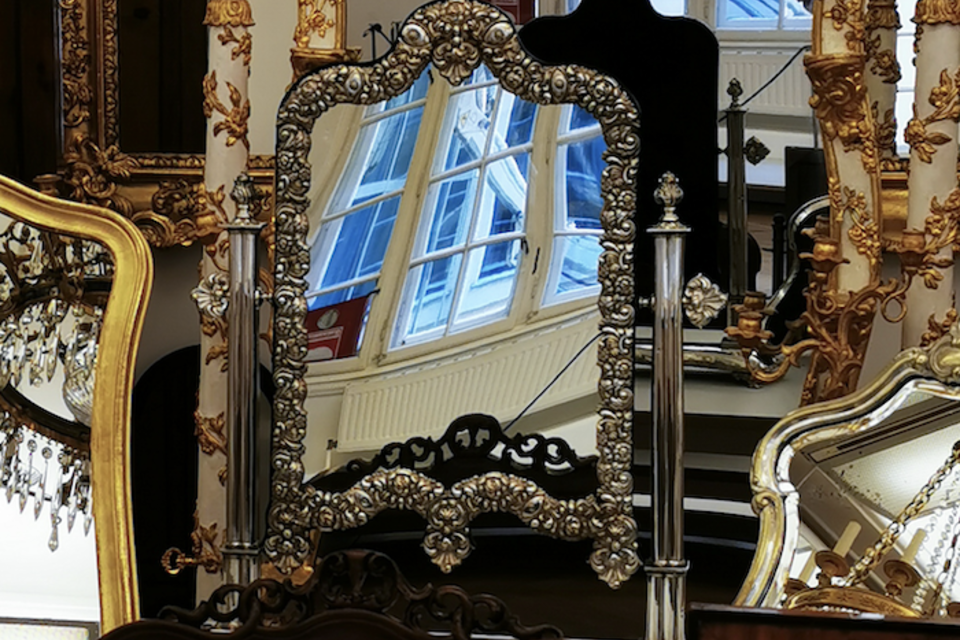 Ein eleganter Spiegel mit kunstvollen Verzierungen aus Silber und Gold. Im Hintergrund sind weitere Spiegel und Fenster zu sehen. | © Irmgard-Unger-Eisele.