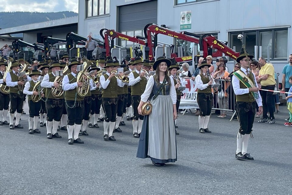 Eine Gruppe von Musikern in traditioneller Tracht zieht durch die Straße. Im Hintergrund sind Zuschauer versammelt, die das Ereignis beobachten. | © Musikverein Ratten