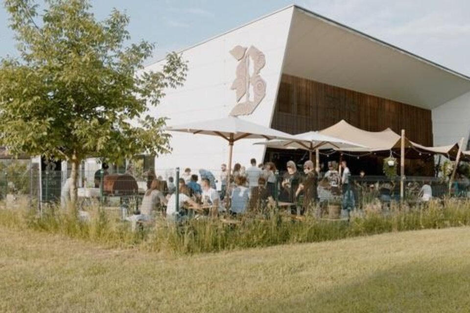 Ein modernes Café mit Außenbereich und vielen Gästen. Der Raum ist von einer grünen Wiese und Bäumen umgeben. | © Brauhaus Bevog