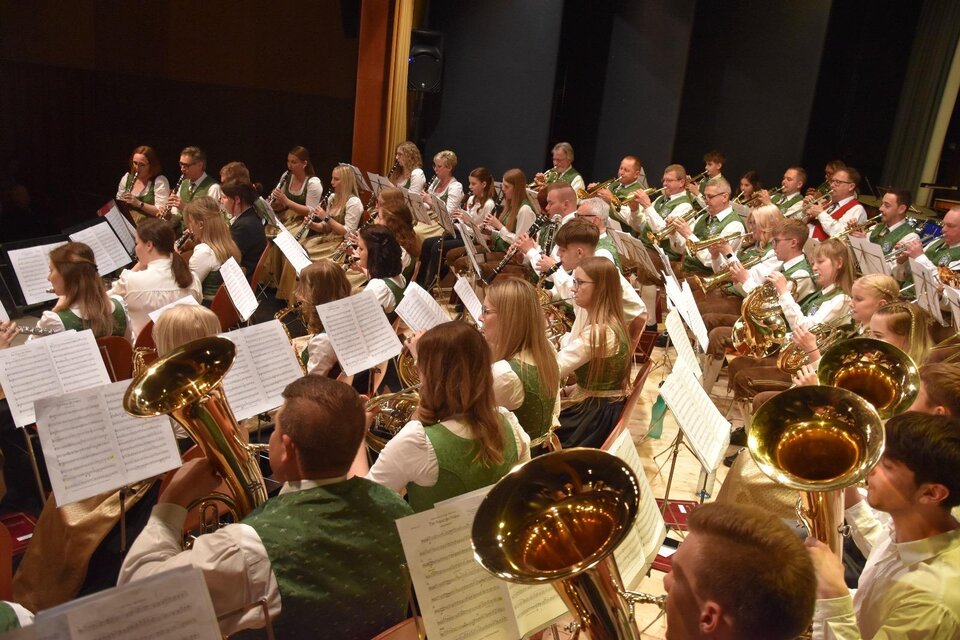Ein großes Blasorchester spielt auf der Bühne. Die Musiker tragen traditionelle Trachten und sind auf ihre Noten konzentriert. | © MMK Bad Waltersdorf