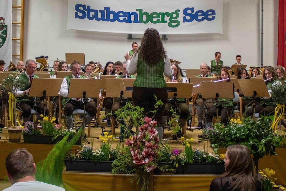 Eine große Gruppe von Musikern in traditionellen grauen Uniformen steht auf einer Treppe. Einige Personen sitzen vorne und halten Musikinstrumente. | © Musikverein Stubenberg