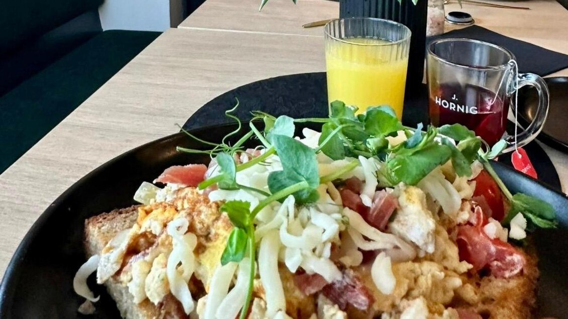 Ein köstlicher Teller mit Rührei auf Brot, garniert mit frischem Gemüse und Kräutern. Dazu ein Glas Orangensaft und eine Tasse Tee. | © Gipfelmomente GmbH