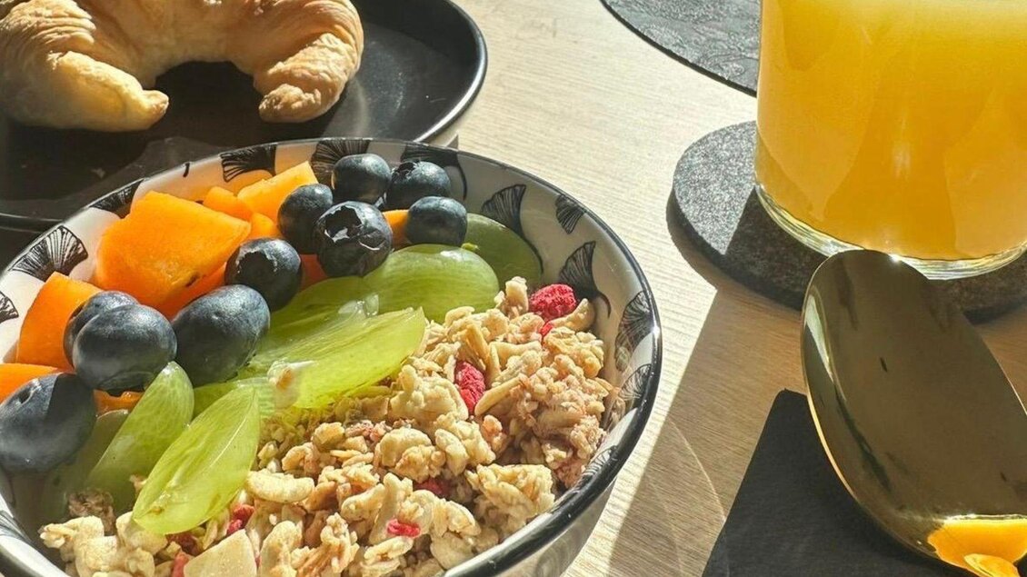 Ein gesundes Frühstück mit Müsli, frischem Obst und einem Croissant. Dazu ein Glas O-Saft auf einem Tisch. | © Gipfelmomente GmbH