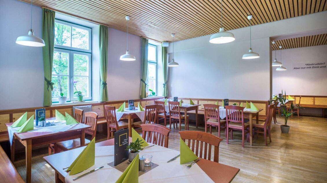 Ein helles Restaurant mit Holzmöbeln und grünen Dekorationen. Die Tische sind für Gäste vorbereitet und das Licht ist freundlich. | © JUFA Hotel Grundlsee