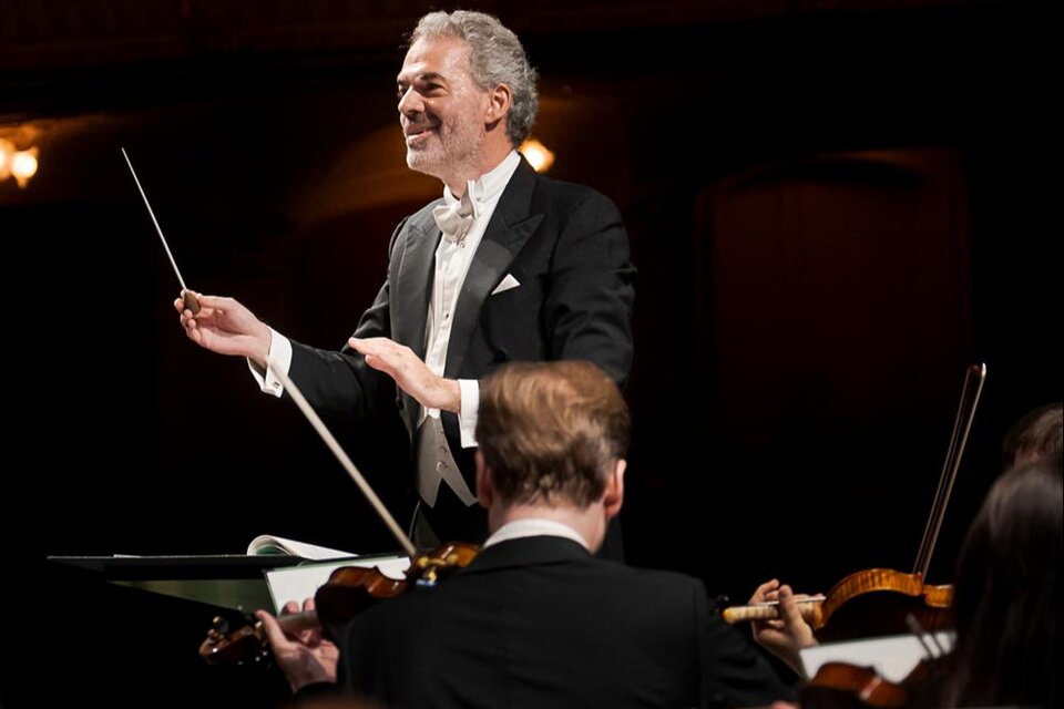Ein Dirigent führt ein Orchester mit Leidenschaft. Im Hintergrund sind Musiker mit verschiedenen Instrumenten zu sehen. | © _Oper Graz