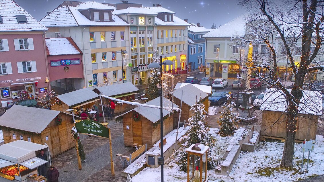 Ein malerischer Weihnachtsmarkt in einer Stadt mit schneebedeckten Ständen. Die Umgebung ist festlich beleuchtet und es liegt Schnee auf den Dächern. | © Stadtgemeinde Friedberg