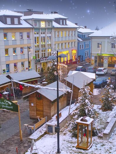 Ein malerischer Weihnachtsmarkt in einer Stadt mit schneebedeckten Ständen. Die Umgebung ist festlich beleuchtet und es liegt Schnee auf den Dächern. | © Stadtgemeinde Friedberg