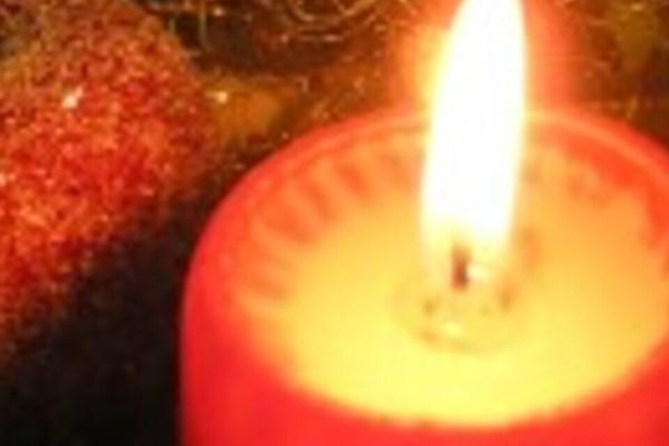 Eine rote Kerze brennt sanft und spendet warmes Licht. Im Hintergrund sind glitzernde Elemente sichtbar. | © THVL