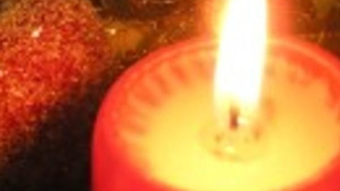 Eine rote Kerze brennt sanft und spendet warmes Licht. Im Hintergrund sind glitzernde Elemente sichtbar. | © THVL