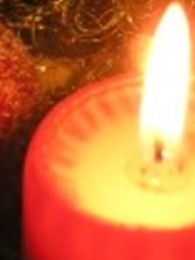 Eine rote Kerze brennt sanft und spendet warmes Licht. Im Hintergrund sind glitzernde Elemente sichtbar. | © THVL