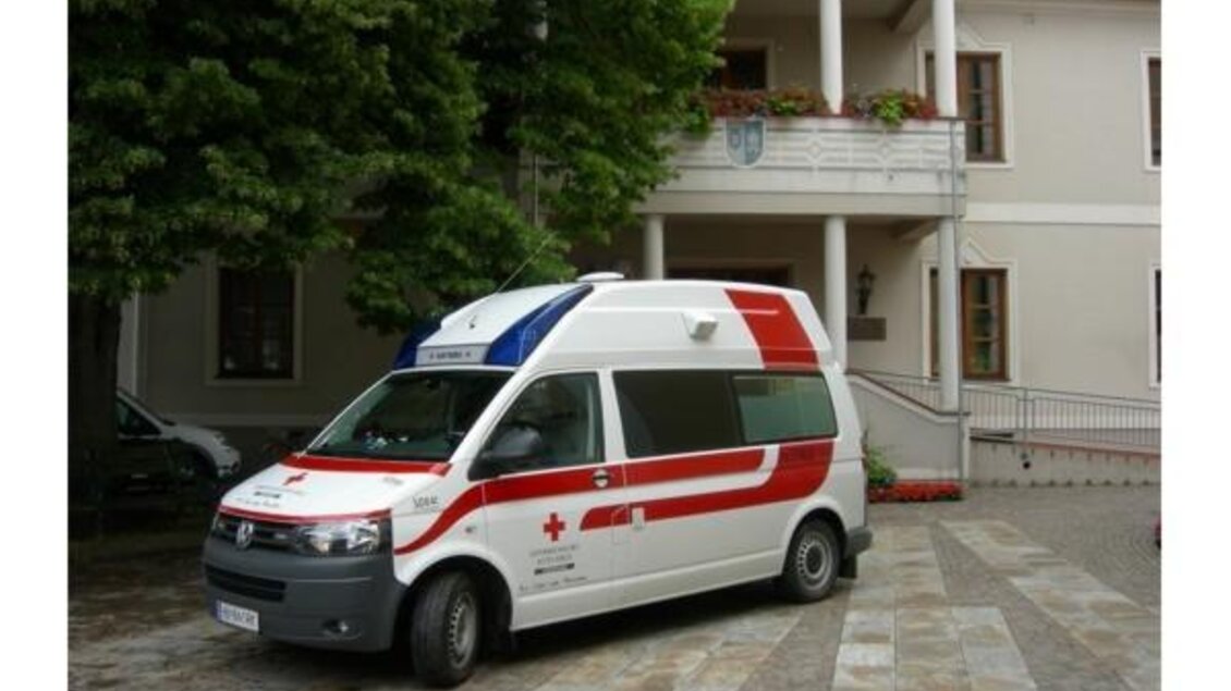 Ein Rettungswagen steht vor einem Gebäude. Das Fahrzeug hat eine rote und weiße Lackierung mit einem roten Kreuz. | © Josef Lederer