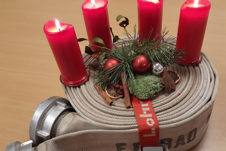 Eine Feuerwehrschlauchrolle mit roten Kerzen und festlicher Dekoration. Der Schlauch ist mit einer roten Schleife und kleinen Weihnachtsaccessoires geschmückt. | © FF Bad Waltersdorf