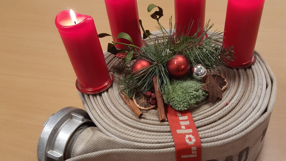 Eine Feuerwehrschlauchrolle mit roten Kerzen und festlicher Dekoration. Der Schlauch ist mit einer roten Schleife und kleinen Weihnachtsaccessoires geschmückt. | © FF Bad Waltersdorf