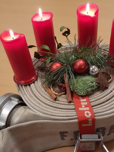 Eine Feuerwehrschlauchrolle mit roten Kerzen und festlicher Dekoration. Der Schlauch ist mit einer roten Schleife und kleinen Weihnachtsaccessoires geschmückt. | © FF Bad Waltersdorf