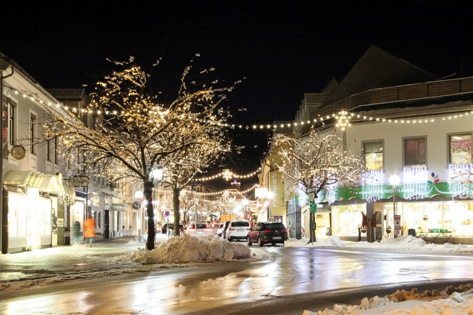 Eine charmante Straße mit festlichen Lichtern und verschneiten Bäumen bei Nacht. Die Gebäude sind hell erleuchtet und schaffen eine gemütliche Atmosphäre.
