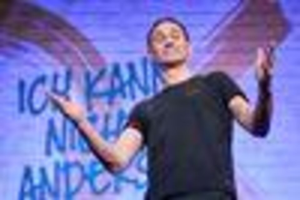 Ein Mann steht auf der Bühne und spricht interessiert sein Publikum an. Im Hintergrund ist ein lebendiges Wandbild mit dem Text „Ich kann nichts anderes“ zu sehen. | © ©MarkusWache