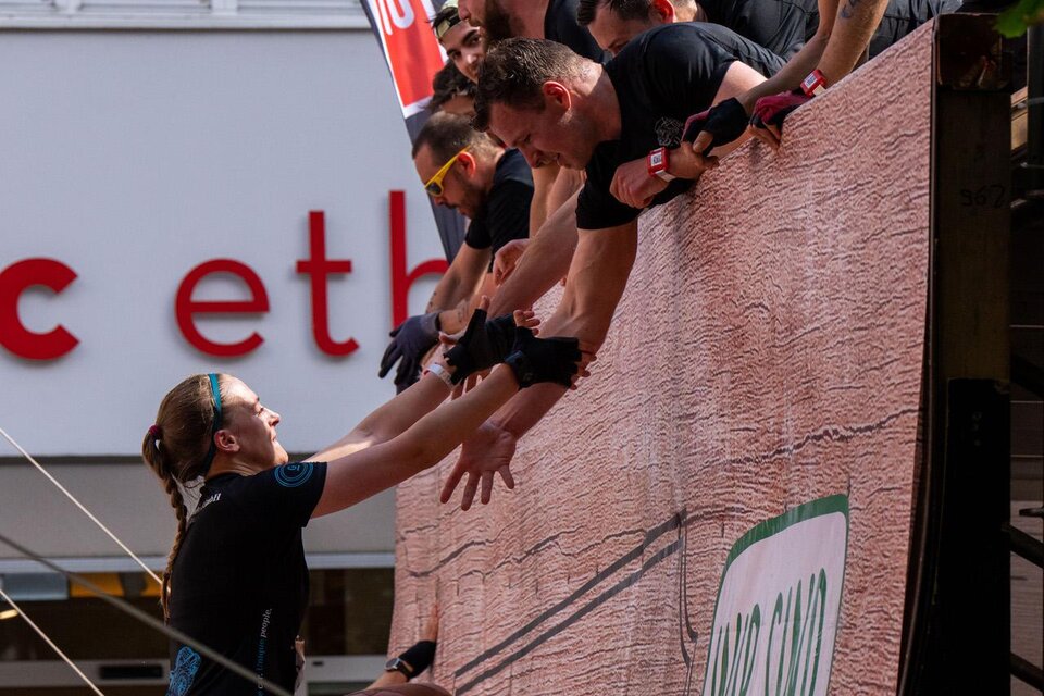 Ein aufregendes Wettkampf-Event, bei dem Teilnehmer eine Wand erklimmen. Die Zuschauer beobachten gespannt, während die Athleten sich gegenseitig helfen.