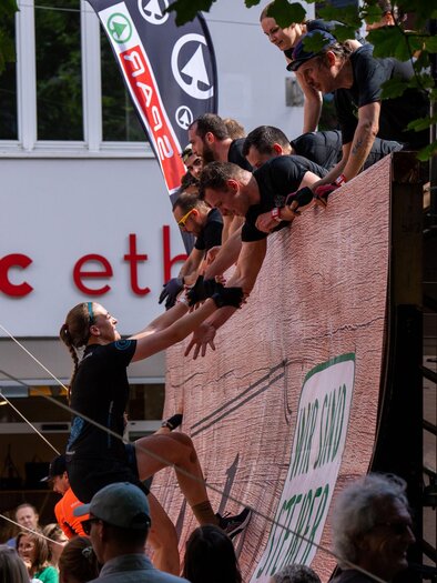An exciting competitive event where participants climb a wall. The spectators watch eagerly as the athletes help each other.