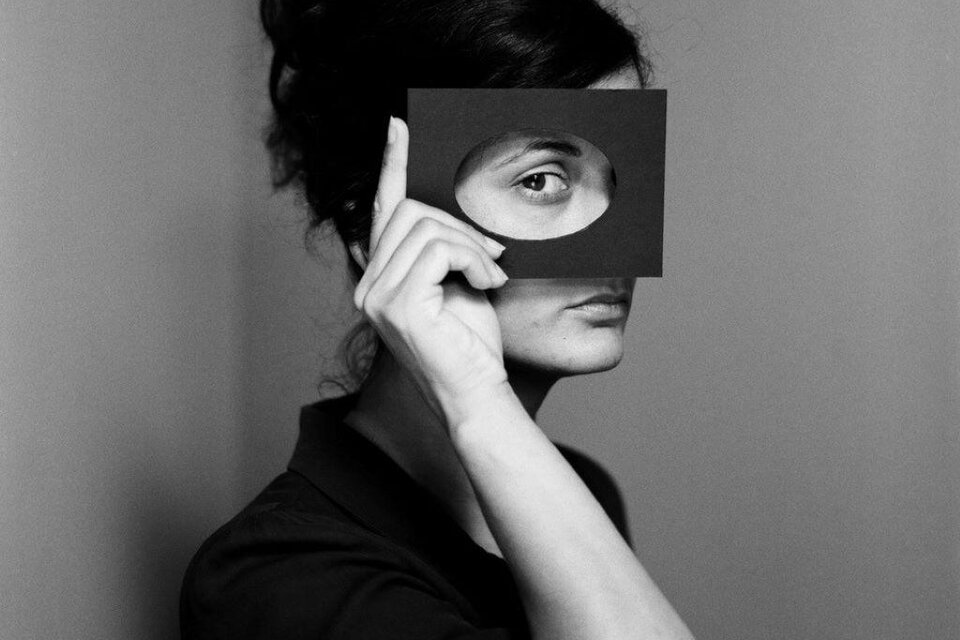 Eine Frau hält ein schwarzes Rechteck vor ihr Gesicht. Sie schaut durch das Loch und hat eine nachdenkliche Miene. | © Judith Stehlik